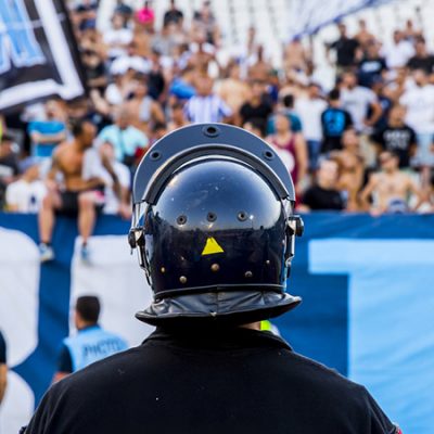 Policía Observando Una Tribuna Con Hichas De Futbol Cantando