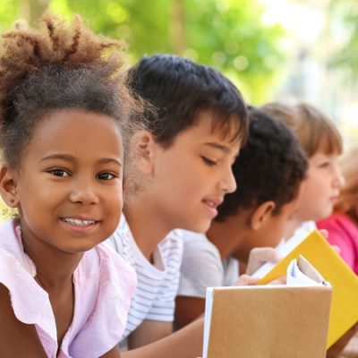 Niña Inmigrante Mirando Un Libro Integrada Con Otros Niños