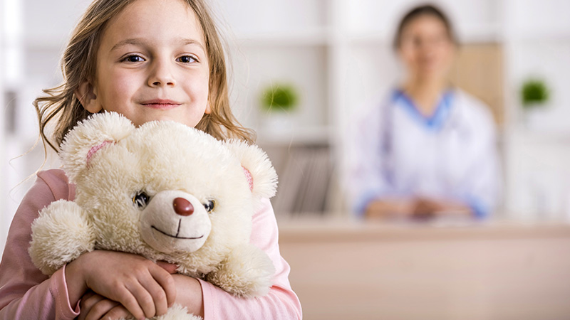 niña mirando al frente, en el fondo se ve una persona en un mostrador en un centro de asistencia de salud